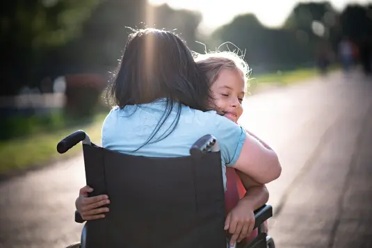 Mädchen umarmt glücklich Frau im Rollstuhl